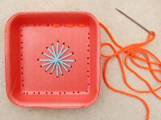 an orange tray with a blue flower on it next to a pair of knitting needles