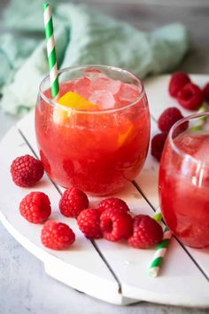 two glasses filled with raspberry lemonade next to some raspberries on a plate