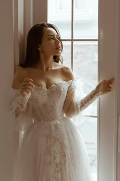 a woman in a wedding dress looking out the window