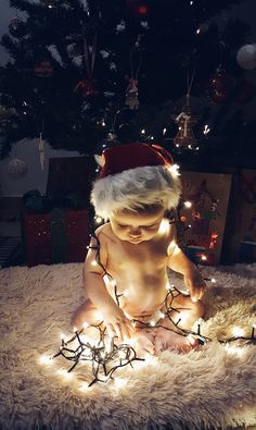 a baby wearing a santa hat sitting on top of a rug next to a christmas tree