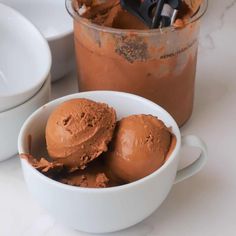 three scoops of chocolate ice cream in a white bowl next to a container with spoons