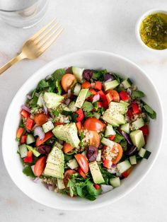 a salad with cucumbers, tomatoes, olives and other vegetables in a white bowl