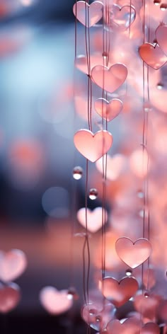 pink hearts hanging from strings in front of a blurry background with lights and bubbles