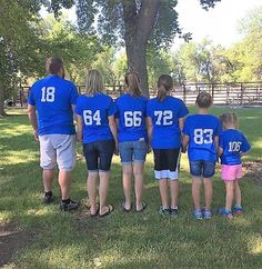 a group of people in blue shirts standing next to each other near a tree and fence