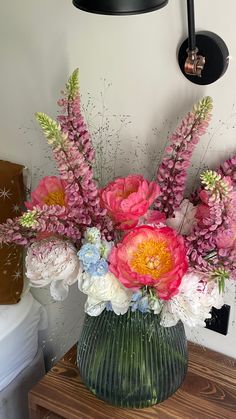 a vase filled with pink and white flowers on top of a wooden table next to a bed