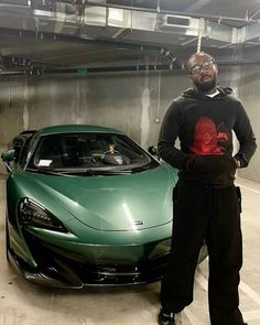 a man standing next to a green sports car in a parking garage with his hands on his hips