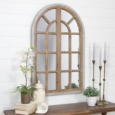 a wooden table topped with a vase filled with flowers and candles next to a window