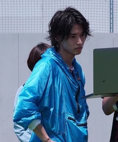 a man in blue raincoat using a laptop computer while standing next to other people