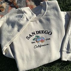 This is an original classic San Diego Est. 1769 California Design from Onlythegoodthingz. A beautiful representation of San Diego, where the city and beach meets 🏙️🏝️🌊 Design is embroidered as ordered on Gildan Heavy Blend Hoodies and Crewnecks see photos for sizing and product care. I personally wear Gildan Brand crewnecks and hoodies, once they are done in the dryer, I recommend hanging them up like most clothes to avoid wrinkles. Thank you so much for the love :) San Diego Clothes Outfits, San Diego Sweatshirt, Crew Neck Sweatshirt Embroidery, Style Inspo Winter, California Hoodie, Classic Embroidery, California Sweatshirt, School Bag Essentials, California Design