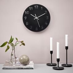 a clock that is on the side of a wall next to candles and a vase