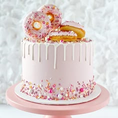 a pink cake with sprinkles and donuts on top