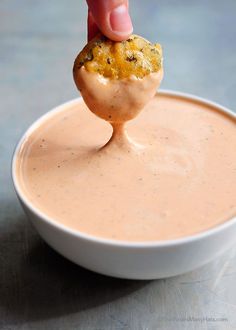 a person dipping something into a bowl of dip with a small cracker in it