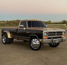 a black and brown truck parked on top of a parking lot next to a field