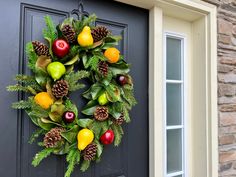 a wreath with fruit and pine cones hanging on the front door to decorate an entrance