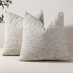 two white pillows sitting on top of a couch next to a potted green plant