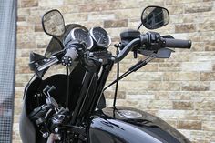 the handlebars and gauges of a motorcycle parked in front of a brick wall