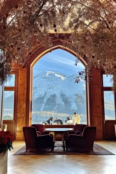 two people sitting at a table in front of an open window with mountains behind them