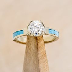 an engagement ring with a blue band and a diamond in the center on top of a wooden stand