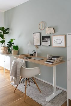 a desk with a computer on top of it next to a white cabinet and potted plant