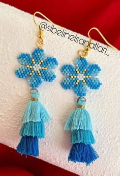 two blue flowers with tassels are hanging from gold earwires on a white napkin