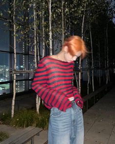 a woman with red hair standing in front of some trees