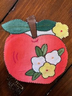 an apple with flowers on it sitting on top of a wooden table next to a piece of cloth