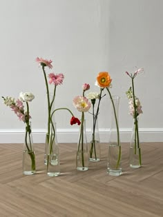 five vases with flowers in them on the floor next to a wall and hardwood floor