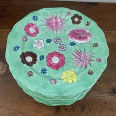 a green bowl with flowers painted on the top and bottom sitting on a wooden floor