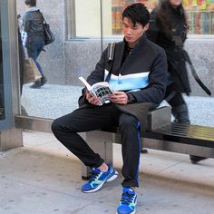 a young man sitting on a bench reading a book in front of a store window