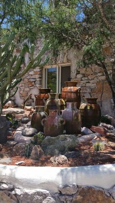 several large vases sitting on top of rocks in front of a building with cactus trees