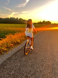 a woman riding a bike down the middle of a road in front of a field