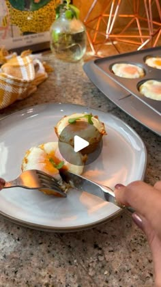 a person holding a knife and fork over some food on a white plate with muffins in the background