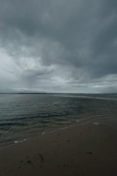 an empty beach with waves coming in to shore and dark clouds over the water on a gloomy day