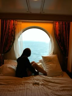 a woman sitting on top of a bed in front of a window with red curtains