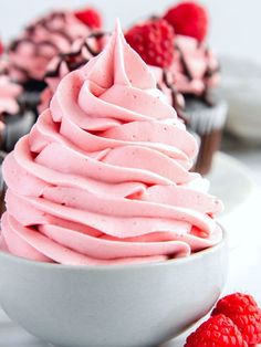 two cupcakes with pink frosting and raspberries in the background on a plate