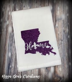 a white dish towel with the state of minnesota in purple glitter, on top of a wooden table