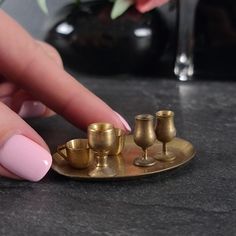 a woman's hand with pink nail polish and gold cups on a black table