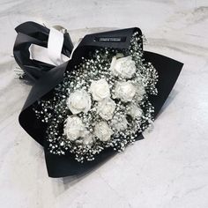 a bouquet of white roses and baby's breath on a black paper wrapper