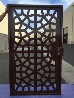 a person is holding up a decorative metal door on the side of a building that has a parking lot in front of it