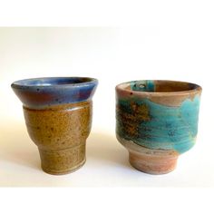 two ceramic cups sitting side by side on a white surface, one with blue and brown glazes