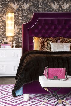 a purple bed with leopard print pillows and a pink handbag on the foot board