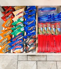 an open drawer filled with snacks and candy bar wrappers on top of a tiled floor