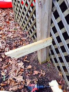 a power drill is laying on the ground next to a wooden fence and some leaves