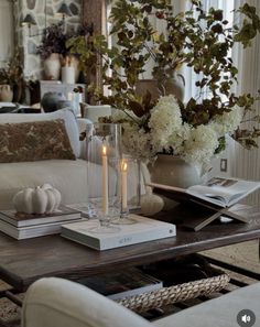 a living room filled with furniture and a table topped with books, candles and flowers