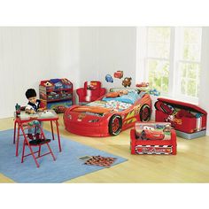 a child's bedroom with cars bed, desk and toy storage bins on the floor