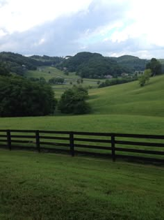 a black fence in the middle of a grassy field with trees and hills in the background