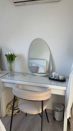 a white desk with a mirror, stool and flower vase on the table in front of it