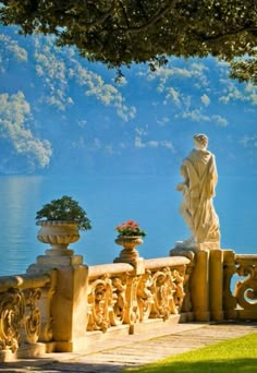 a statue on the edge of a stone wall next to a body of water with mountains in the background