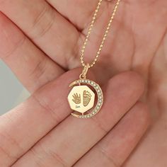 a person holding a gold necklace with a baby's hand and heart on it