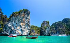 several boats floating on the water near large rocks and cliffs in an ocean with clear blue skies